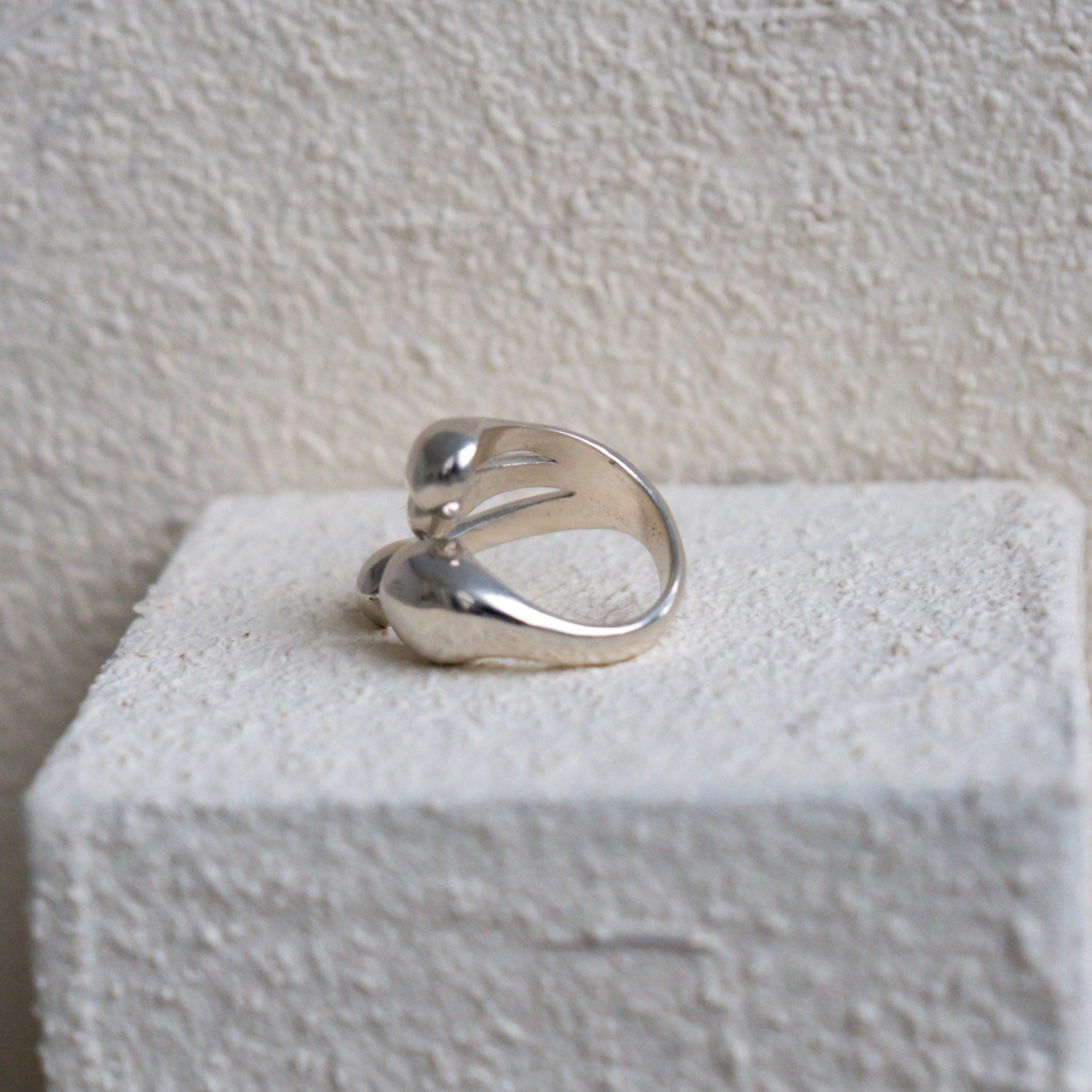 Silver ring on a white cube against a textured beige wall