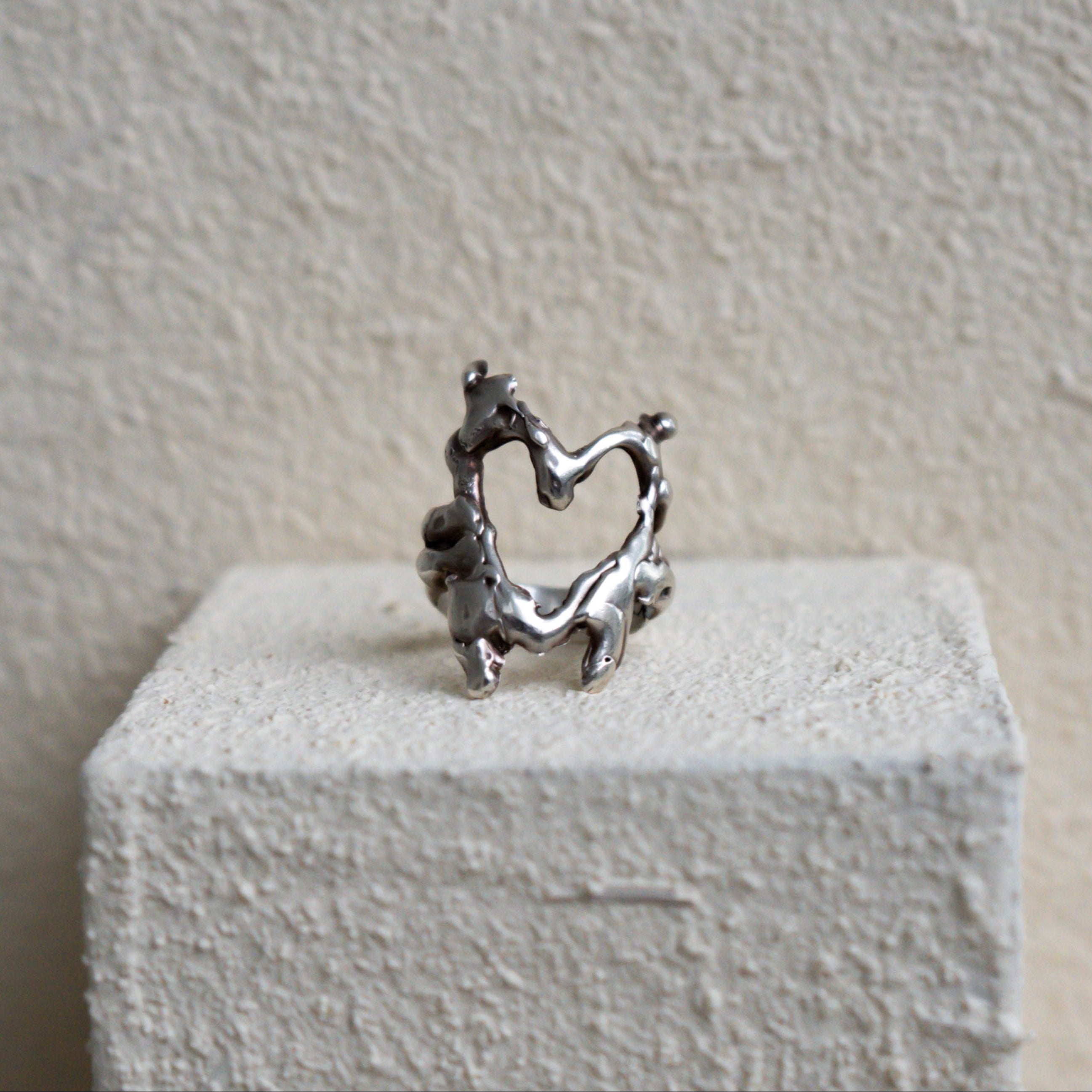 Silver ring with heart design on a white pedestal against a beige wall
