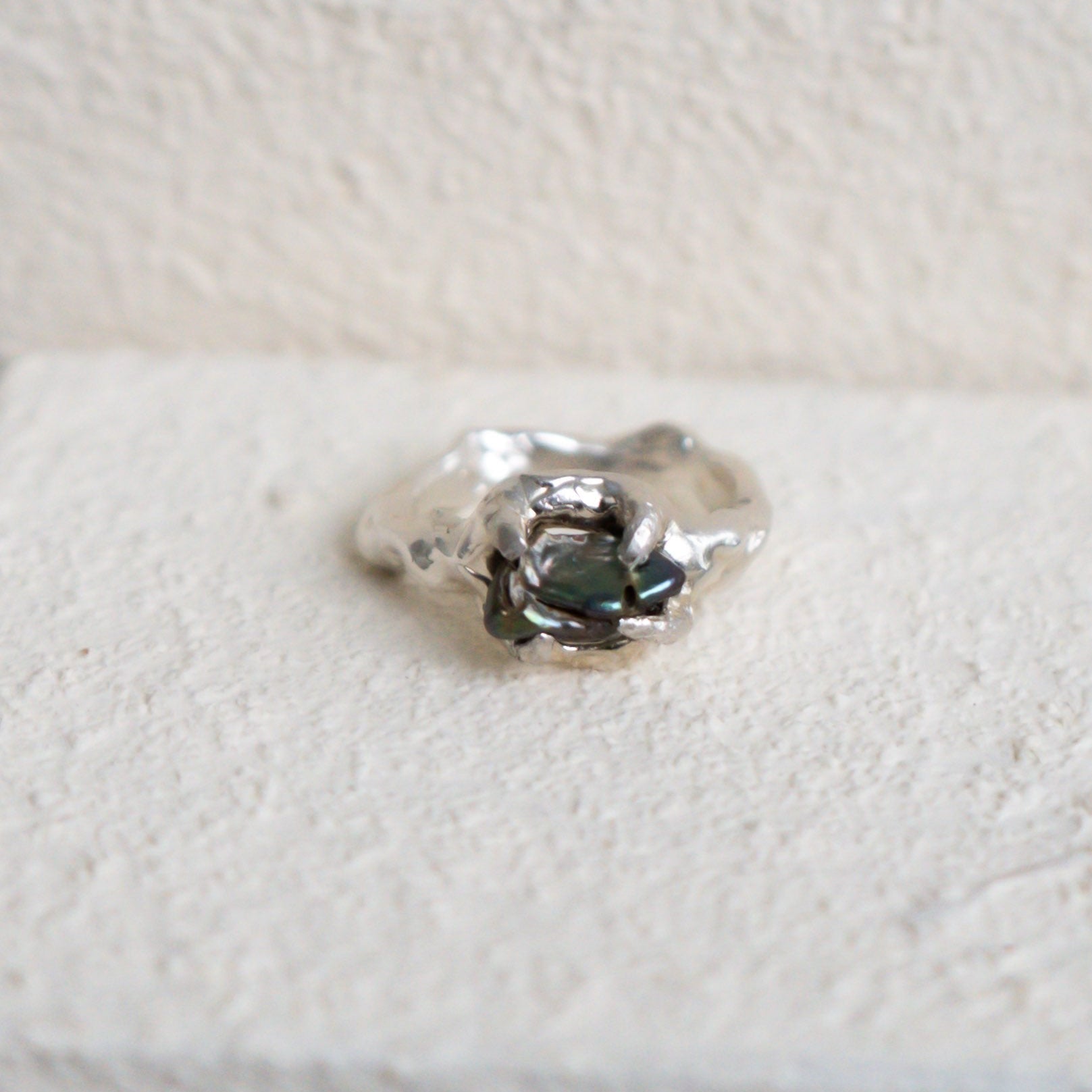 Silver ring with a central green fresh water pearl on a textured white surface