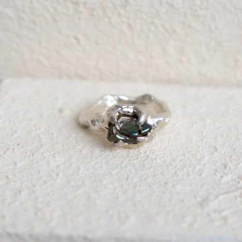 Silver ring with a central green fresh water pearl on a textured white surface