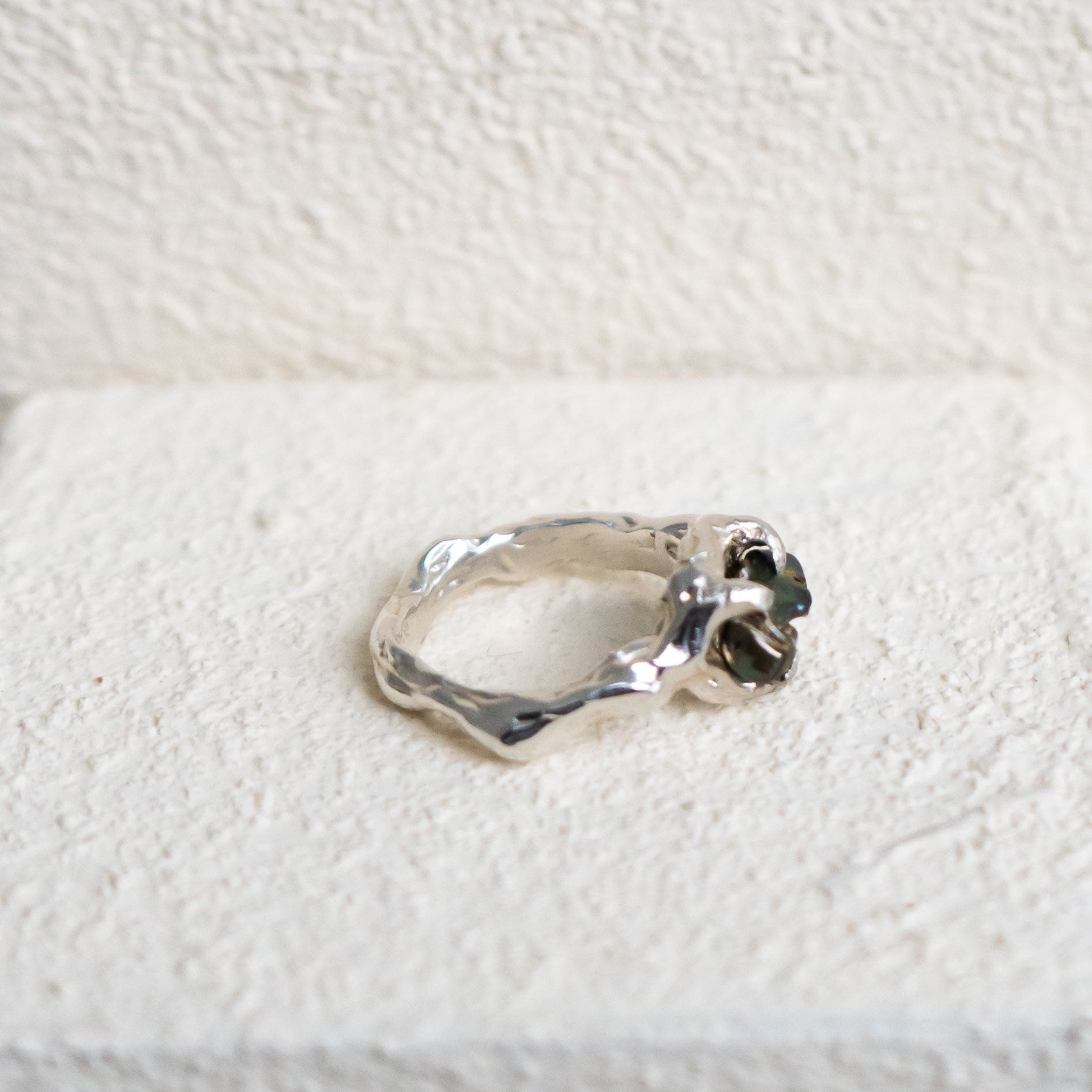 Silver ring with a green fresh water pearl on a textured white surface