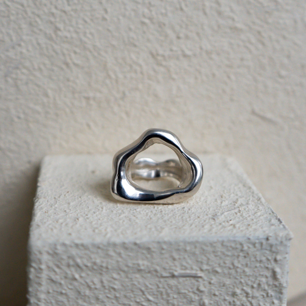Wavy shaped Silver ring on a textured white block with a light gray background